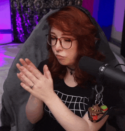 a woman wearing glasses applauds in front of a mic