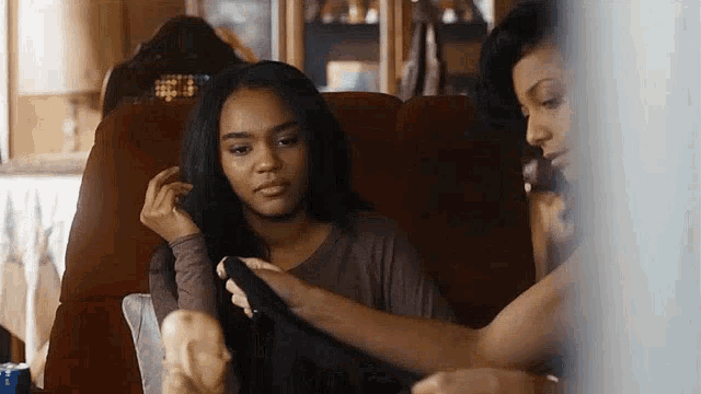 a woman is fixing another woman 's hair while sitting on a couch in a living room .