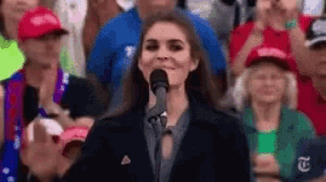a woman is standing in front of a microphone in front of a crowd of people .