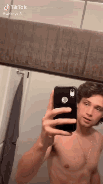 a shirtless man is taking a selfie in a bathroom with his phone .