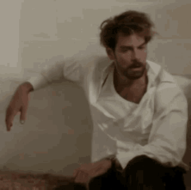 a man in a white shirt is sitting on the floor with his legs crossed .