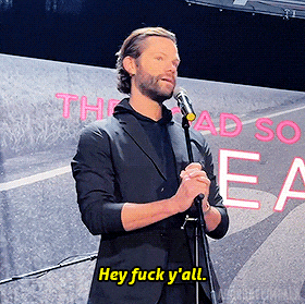 a man in a suit stands in front of a microphone and says hey fuck y 'all