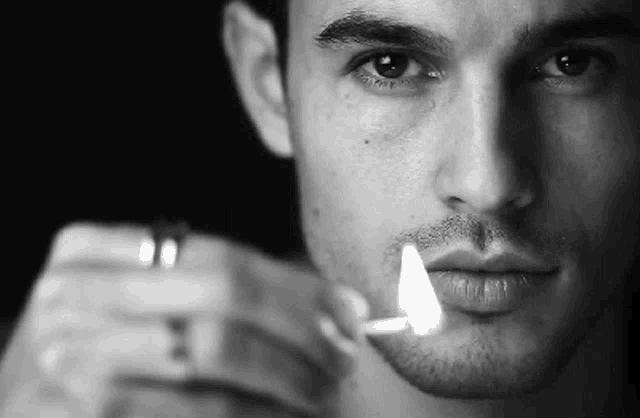 a close up of a man lighting a cigarette with a lighter .