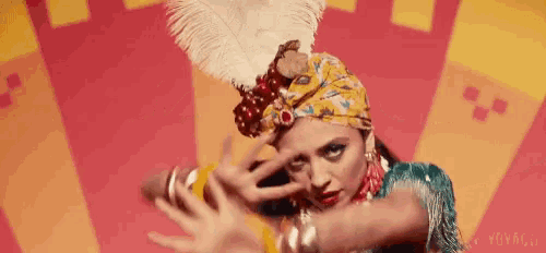 a woman wearing a turban and a feathered headpiece is dancing .
