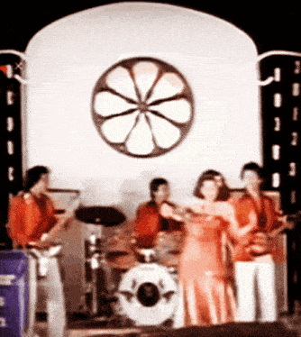 a group of people playing instruments in front of a wall with a flower in the middle