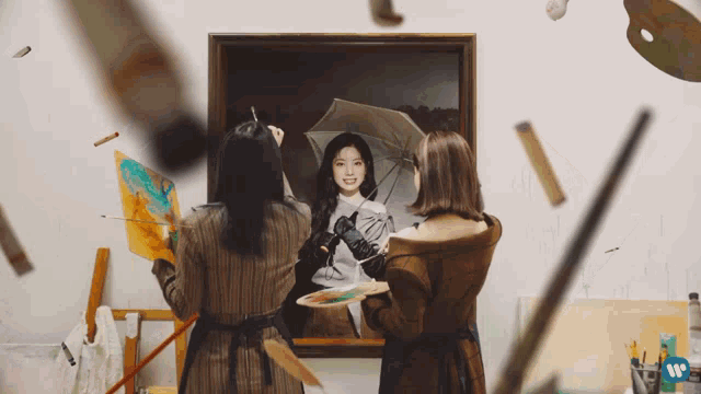 two women are painting a picture of a woman with an umbrella in front of a wall with a w on it
