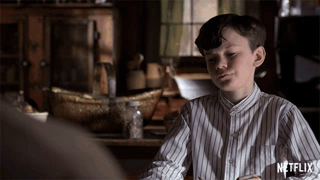 a boy in a striped shirt is sitting at a table with a netflix logo on the bottom right
