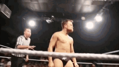 a shirtless wrestler is standing in a wrestling ring with a referee .