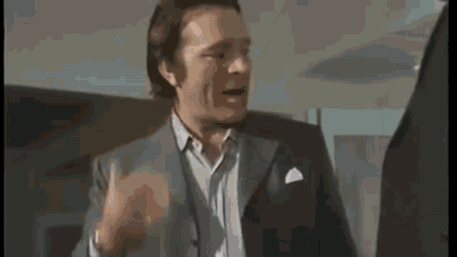a man in a suit is talking to another man in a dark room .