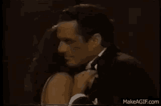a man in a tuxedo is hugging a woman in a black dress .