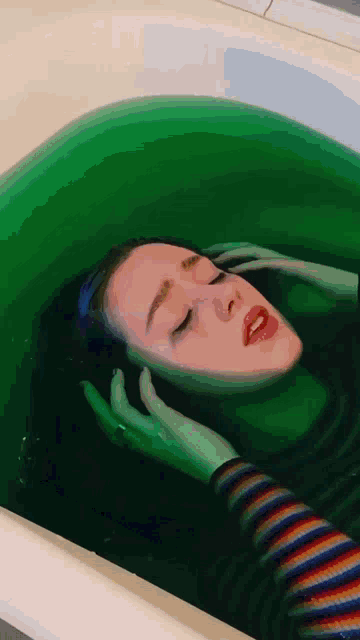 a woman is laying in a bathtub with green water