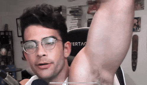 a man wearing glasses shows off his armpit in front of a ferrag chair