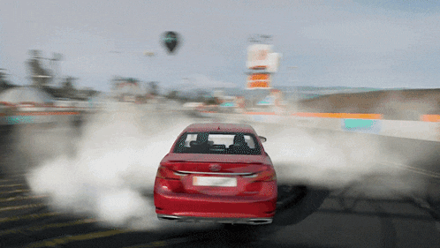 a red car is driving down a road with smoke coming out of its tires