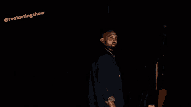 a man with a beard is standing in a dark room with a microphone in his hand .