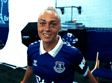 a woman in a blue everton jersey is smiling