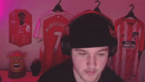 a man wearing headphones and a hat is standing in front of a wall with jerseys on it .