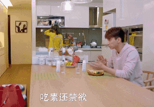 a man sitting at a table in a kitchen with chinese writing on the wall