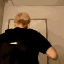 a man in a black shirt is standing in front of a door and looking at the camera .