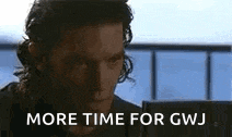 a man with long hair is sitting in front of a computer screen and says `` more time for gwj '' .