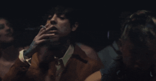 a man with a tattoo on his arm is smoking a cigarette in a dark room