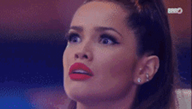 a woman with red lipstick and earrings is looking up at the sky .