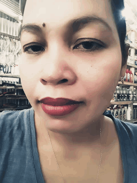 a woman wearing a blue shirt and red lipstick is standing in front of a shelf with bottles of shampoo and conditioner