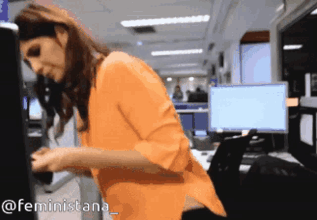 a woman in an orange shirt is standing in front of a computer screen with the hashtag feministana on the bottom