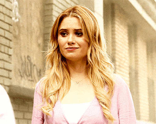 a woman wearing a pink cardigan stands in front of a brick wall