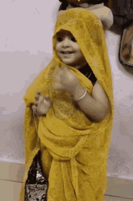 a little girl is wearing a yellow saree and holding a bag .