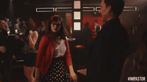 a man and a woman are dancing in a club and the woman is wearing a red cardigan .
