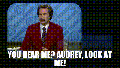 a man in a red suit and tie is standing in front of a television and says you hear me ? audrey look at me .