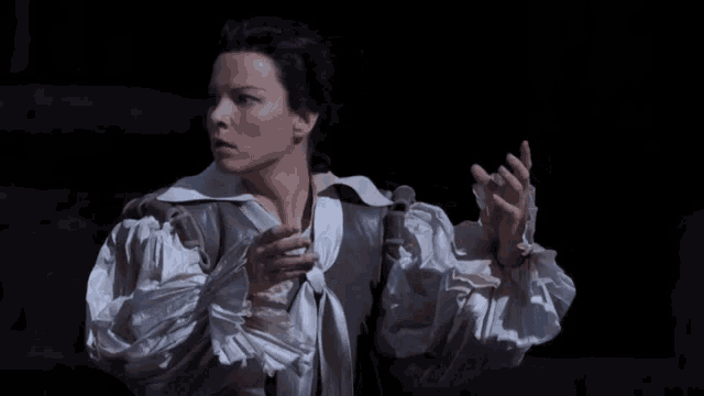 a woman in a white ruffled sleeved shirt holds her hands to her chest