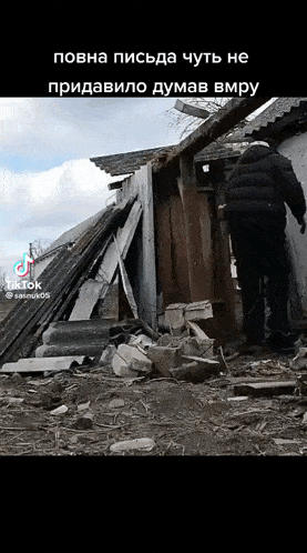 a man in a black jacket is walking in front of a destroyed building ..