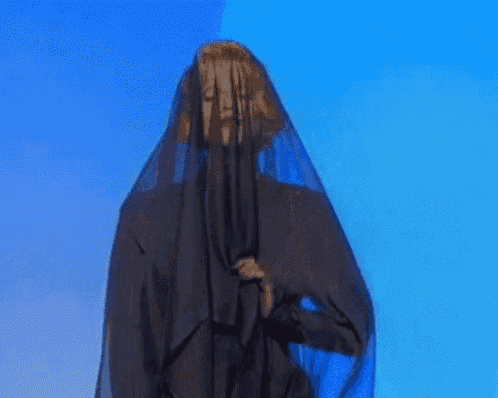 a woman in a black veil is standing in front of a blue background .