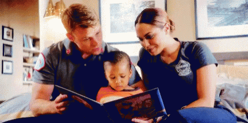 a man and a woman are reading a book to a little boy .