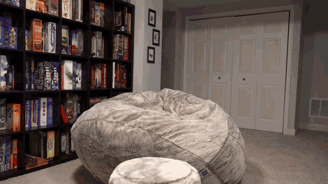a large bean bag chair sits in front of a bookshelf filled with board games including legacy