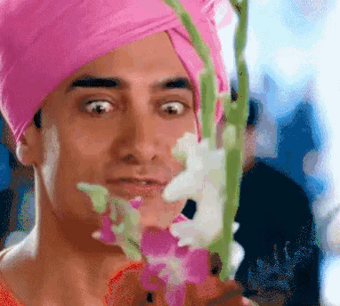 a man in a pink turban is holding a flower in front of his face