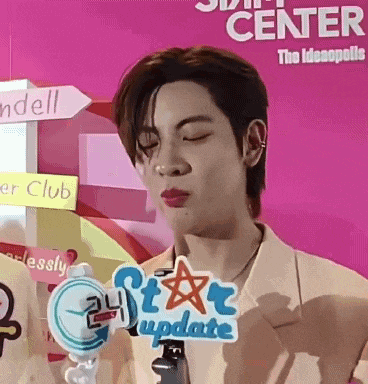 a young man with his eyes closed is standing in front of a pink wall holding a microphone .