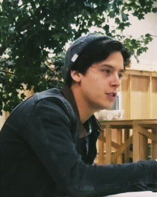 a young man wearing a beanie and a black jacket is sitting in front of a tree .