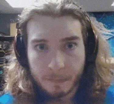 a man with long hair and a beard wearing headphones looks at the camera