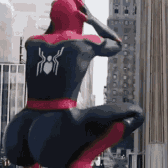a man in a spiderman costume is squatting down on a building .