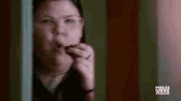 a woman wearing glasses is eating a piece of food while standing in a doorway .