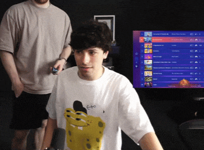 a man wearing a spongebob shirt stands in front of a computer screen