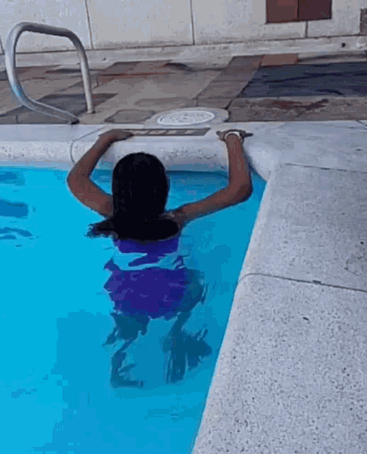 a woman in a purple bikini is swimming in a swimming pool .