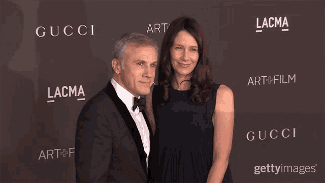 a man and a woman are posing for a picture in front of a wall that says gucci
