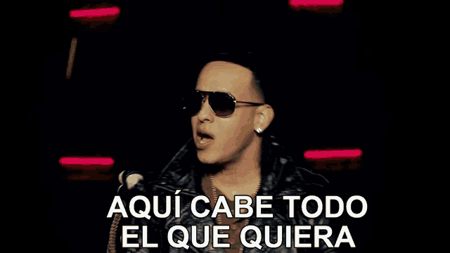 a man wearing sunglasses is standing in front of a neon sign that says aqui cabe todo el que quiera