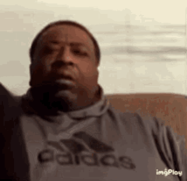 a man is sitting on a couch wearing a gray adidas shirt .