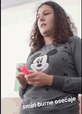 a woman wearing a mickey mouse shirt is holding a pink object ..