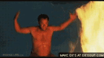 a man without a shirt is standing in front of a fire