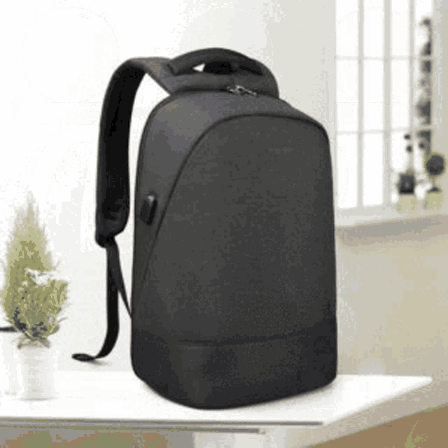 a black backpack is sitting on top of a white table next to a window .